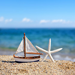 Seaside Park Real Estate coastal lifestyle; toy sailboat and white starfish sitting on a beach with ocean in the background